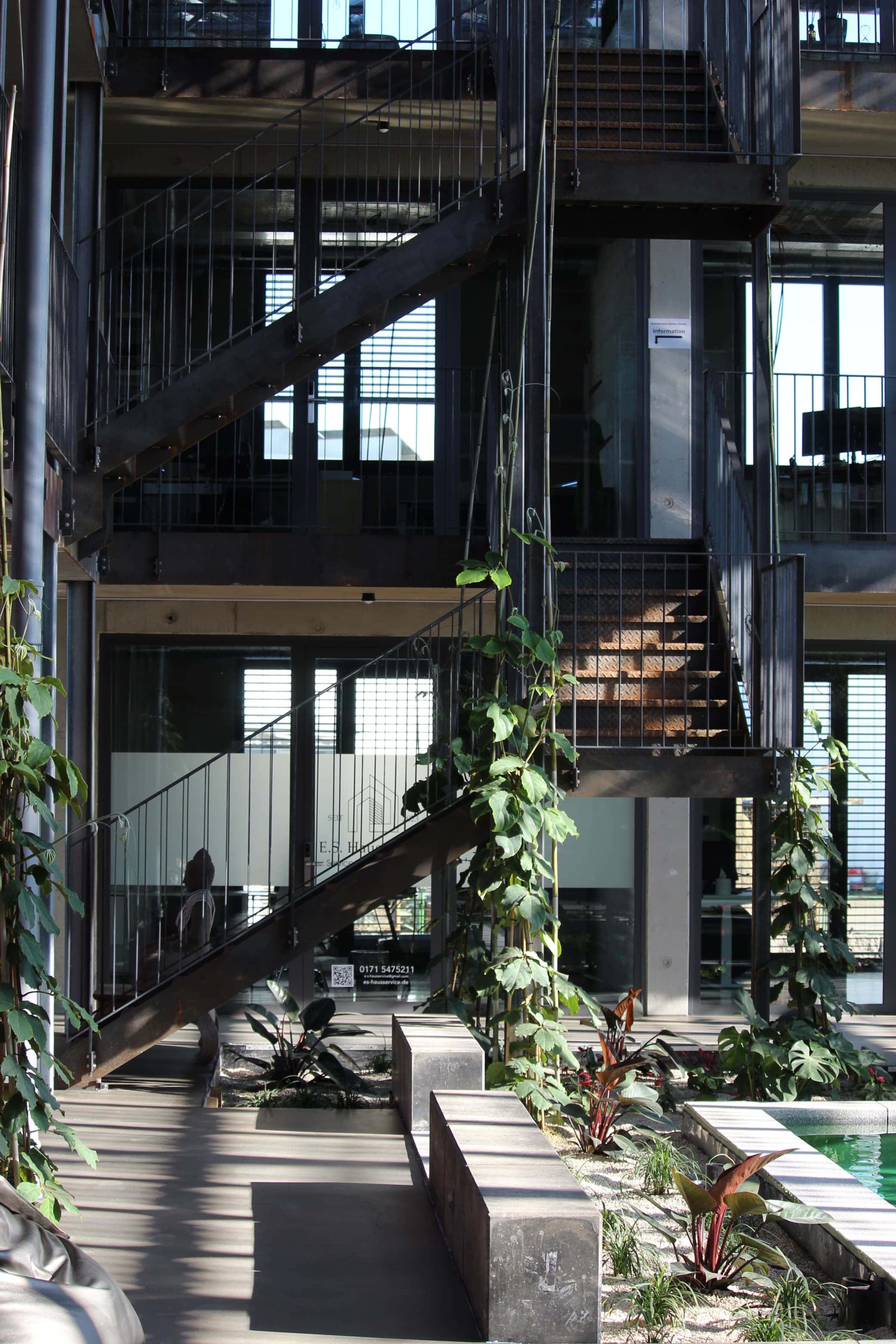 Stahltreppen mit Kletterpflanzen im Atrium, davor Pflanzbeete und Wasserbecken