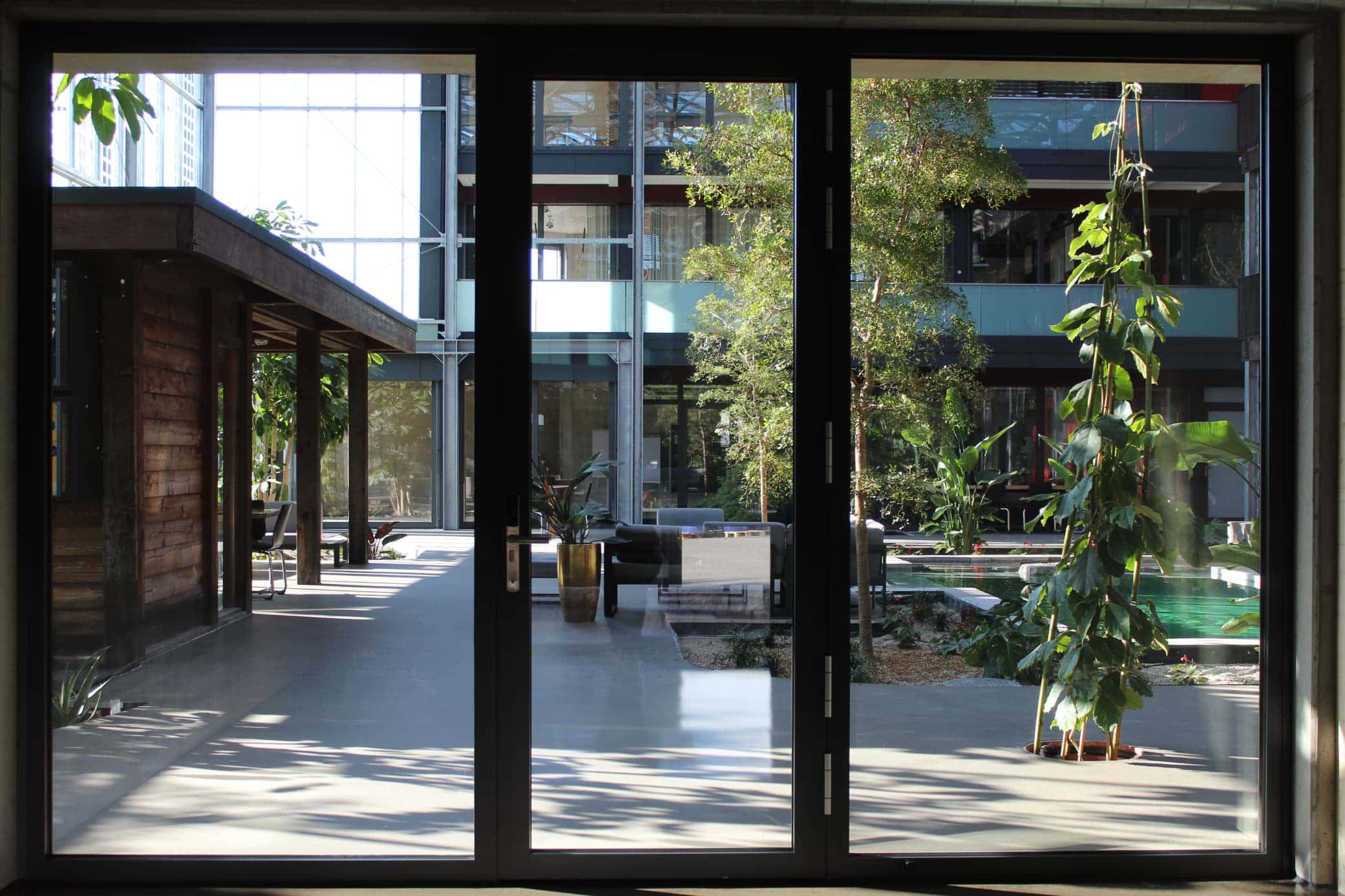Blick durch große Glastüren ins Atrium mit Holzpavillon, Sitzgruppe, Bäumen und Wasserbecken